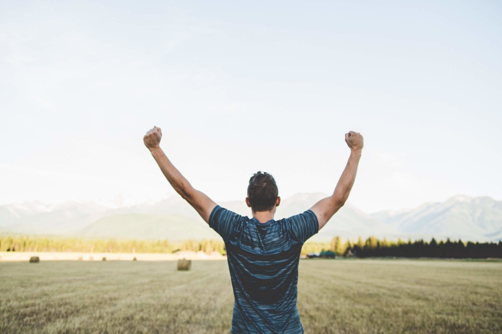 man standing in a field with his hands raised in victory